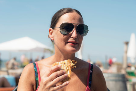 Brunette woman with sunglasses eating sandwich outdoors.の写真素材