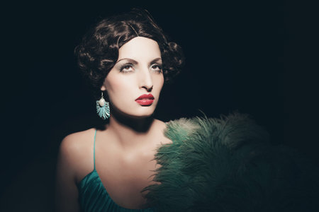 Glamour retro 1920s young woman holding a fan. Against black background.