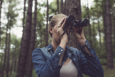 Young woman in forest observing with binocular.の写真素材