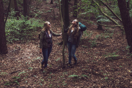 Two twin sister holding tree in forest.