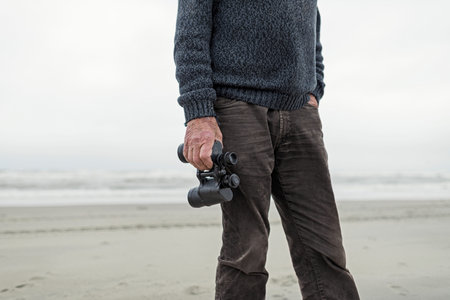 Hand of senior man holding binocular. Standing on beach.