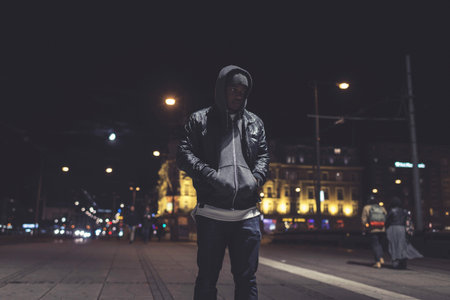 Urban fashion afro man with woolen cap and hoody on the streets of Amsterdam at night.の写真素材