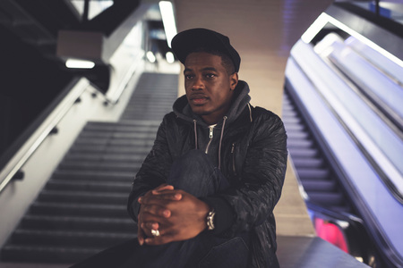 Afro man with black cap sitting on wall in subway station.の写真素材