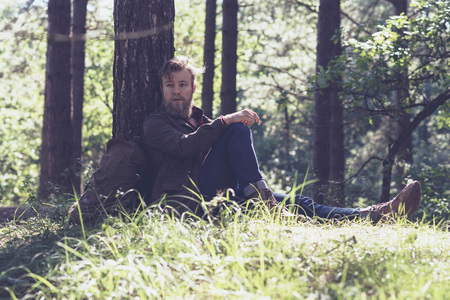 Resting hiker with beard in forest sitting against tree.の写真素材