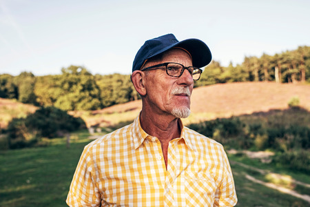 Senior man with beard and cap outdoors in park.の写真素材