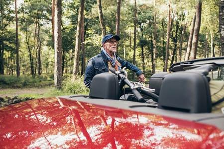 Senior man standing next to cabriolet with bicycle on back seat.の写真素材