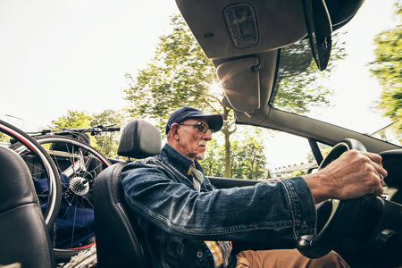 Wide angle shot of senior man driving convertible with bicycle on back seat.の写真素材