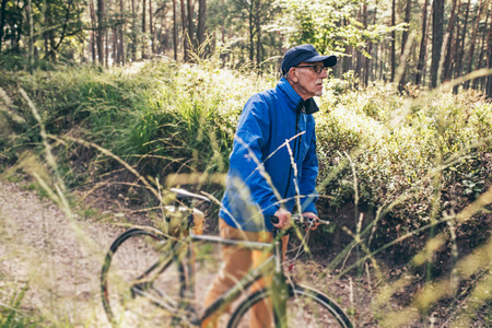 Active senior man walking with bicycle on forest trail.の写真素材