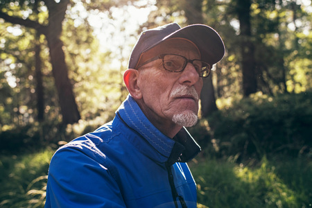 Retired active man with cap in summer forest. Backlit.の写真素材