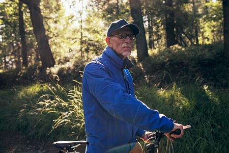 Backlit retired man standing in forest with bicycle.の写真素材