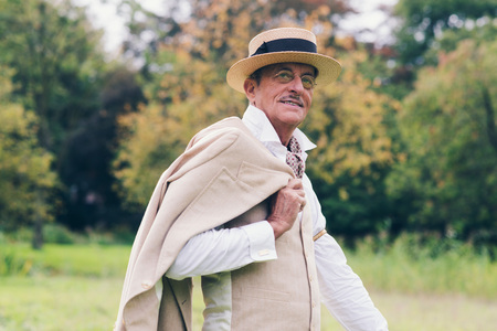 Smiling senior vintage businessman holding jacket over shoulder standing in garden.の写真素材