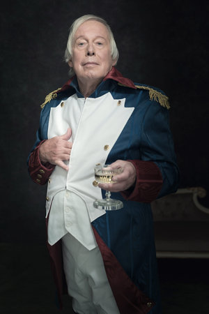 Official portrait of senior man dressed in historical emperor costume. Studio shot against dark...
