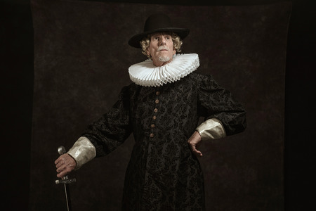 Official portrait of historical governor from the golden age. Standing with sword. Studio shot against dark wall.の写真素材