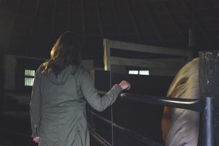 Rear view of woman standing at fence in stable.の写真素材