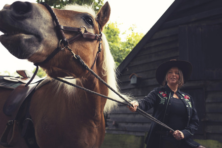 Woman dressed in western style standing with horse at barn.の写真素材