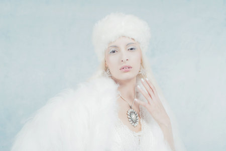 Snow Queen Fashion in White Fur Against Light Blue Wall.