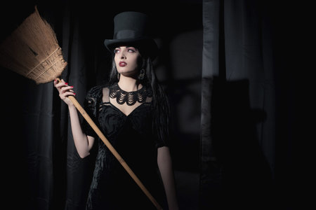 Dark mysterious witch fashion woman. Black curtains with window shadow on wall.