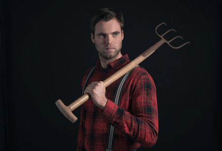 Farmer in red checkered shirt and suspenders holding pitchfork.の写真素材