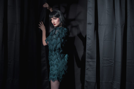 Dark witch fashion woman holding curtain. Standing in dark room.