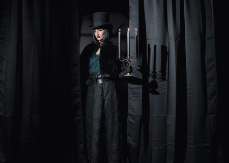 Witch gothic fashion woman wearing black cape and hat. Holding candlestick.の写真素材