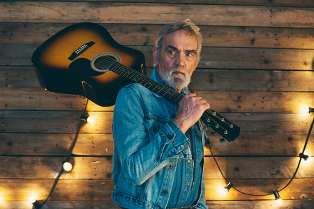 Senior musician with beard holding acoustic guitar on his shoulder.の写真素材