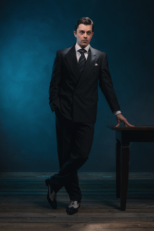 Retro 1940s business man in suit and tie standing next to empty desk.の写真素材