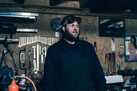 Man with beard wearing overall and goggles in workplaceの写真素材