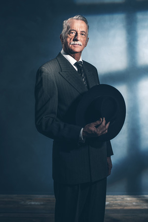 Retro 1940 senior businessman holding hat standing in room.の写真素材