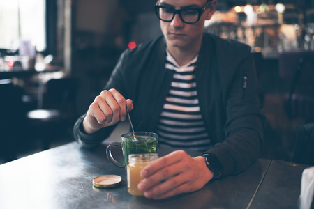 Hipster man with retro glasses putting honey in fresh mint teaの写真素材