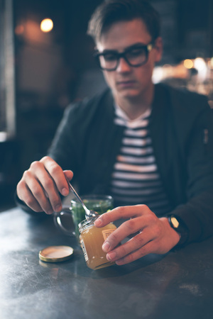 Man in cafe with spoon taking honey out of jarの写真素材
