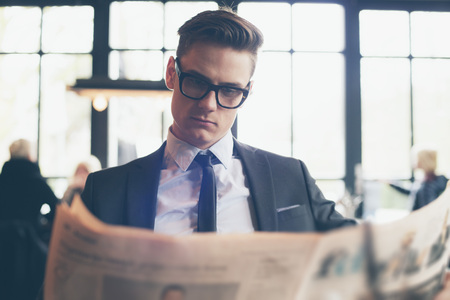 Man in suit with retro glasses reading newspaper in restaurantの写真素材