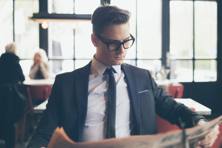 Man in suit with retro glasses reading newspaper in restaurantの写真素材