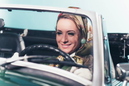 Smiling retro 1960s fashion woman with headscarf driving sports car.