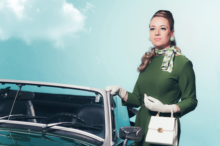 Retro 60s woman in green dress standing next convertible car.の写真素材