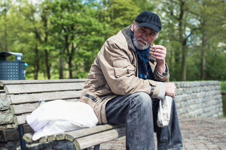 Homeless man smoking cigarette on bench in park.の写真素材