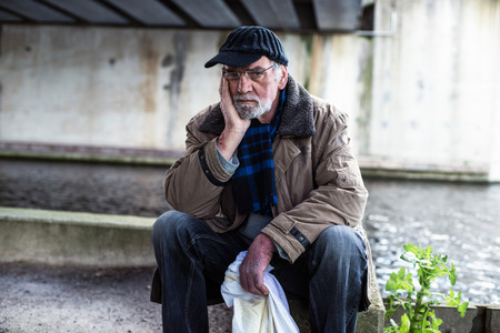 Depressed homeless man sitting on concrete wall under bridge.の写真素材