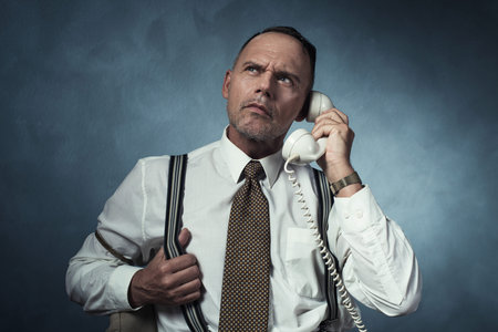 Angry retro 1940 man on the phone sitting on chair in room.