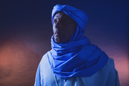 Side view of berber man in night light wearing blue turban with white robe. Studio shot.の写真素材
