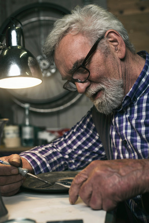 Concentrated senior man repairing tin plate in workshop.の写真素材