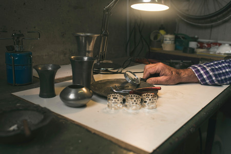 Senior male hand holding magnifying glass on tin plate in workshopの写真素材
