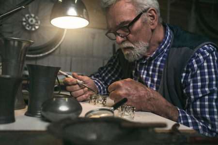 Elderly man soldering metal rings in workshopの写真素材