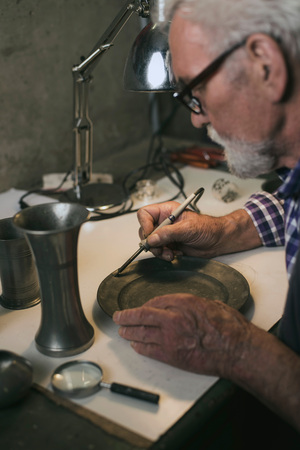 Senior man soldering tin plate in workshop.の写真素材
