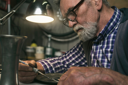 Concentrated senior man repairing tin plate in workshop.の写真素材