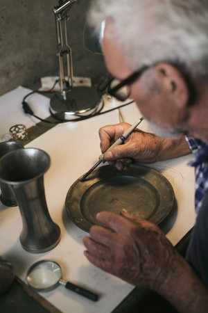 Senior man soldering tin plate in workshop.