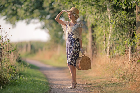 1920s retro fashion woman standing with handbag on rural pathway.の写真素材