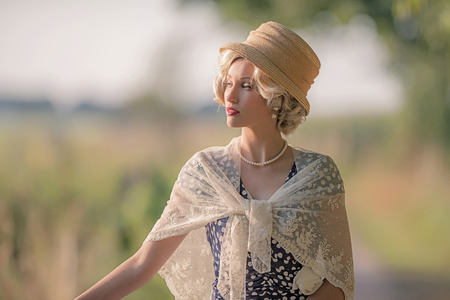 Vintage 1930s fashion woman with hat in rural summer landscape.の写真素材