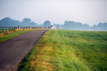 Father and children cycling on rural road in morning mist.の写真素材