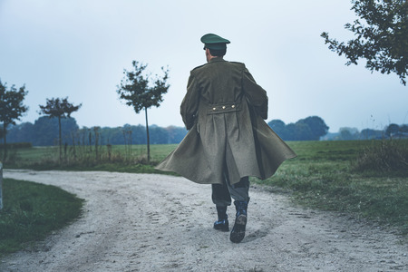 Rear view of vintage 1940s military officer walking on rural road.の写真素材