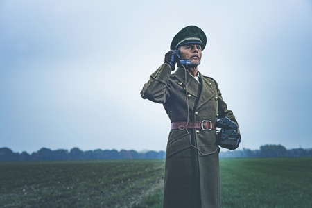 Vintage 1940s military officer calling with field phone while standing on farmland.の写真素材