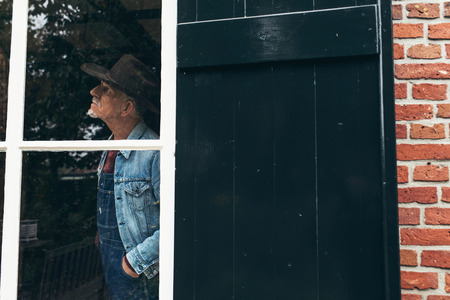 Senior farmer with hat looking out the window of farm.の写真素材
